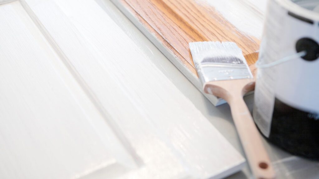 Essential tools for cabinet painting beginners: brush applying white primer to an oak cabinet door