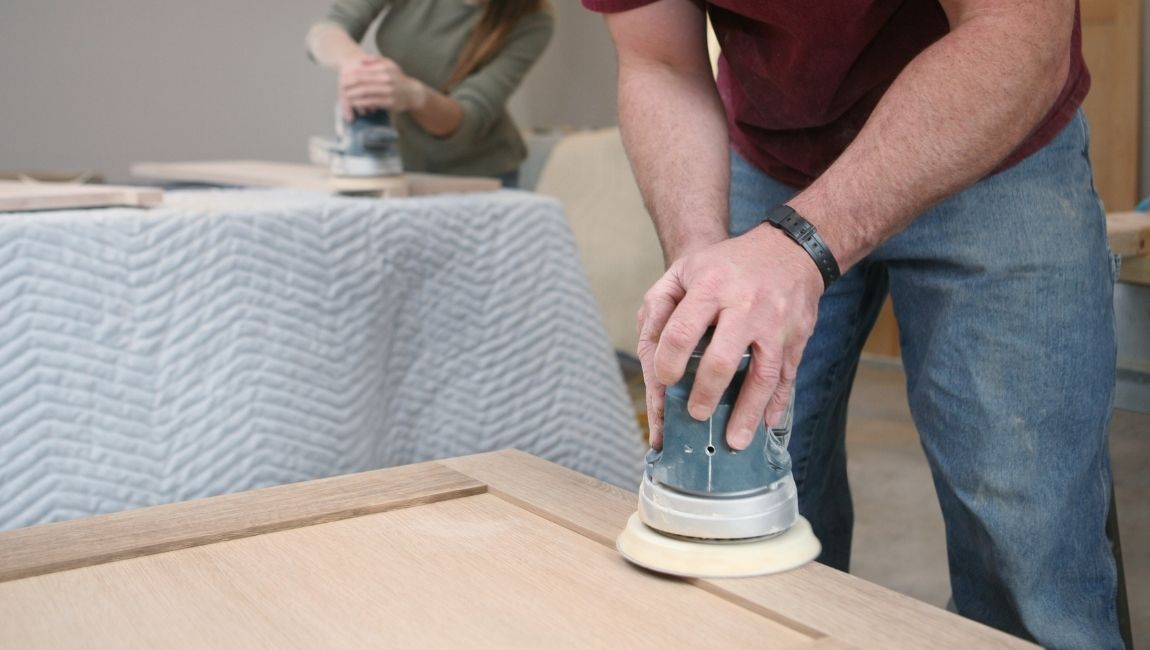 Preparing Cabinets for Painting. Cabinet painting beginners sanding cabinet doors with an orbital sander for better paint adhesion
