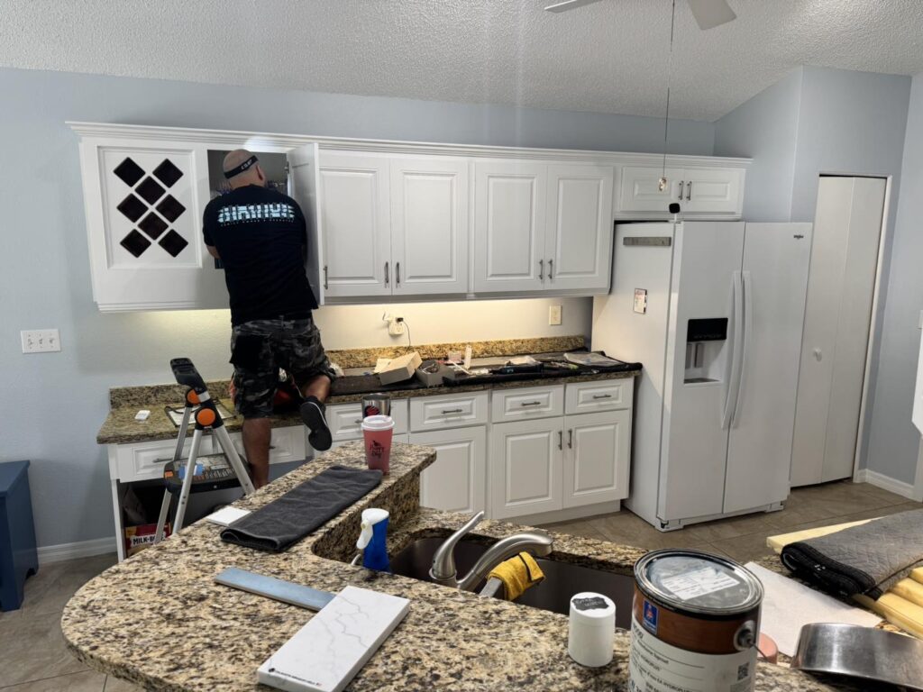 Professional cabinet painting contractor in Florida installing freshly painted white kitchen cabinets with a spray-finish system